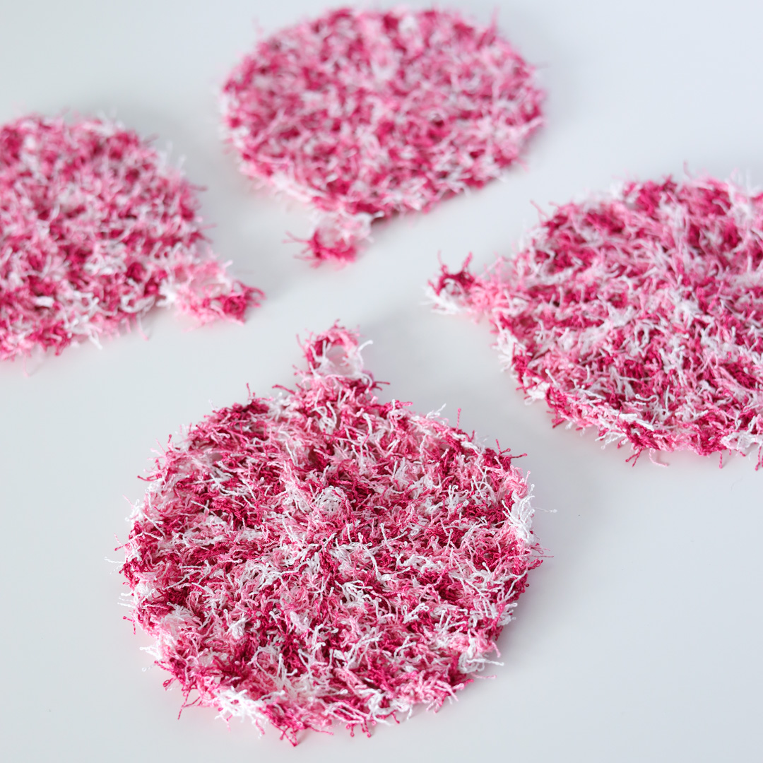 a group of 4 crochet scrubbies made with pink scrubby yarn on a white table