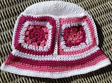 Pink and white granny square crochet bucket hat on wicker background. 