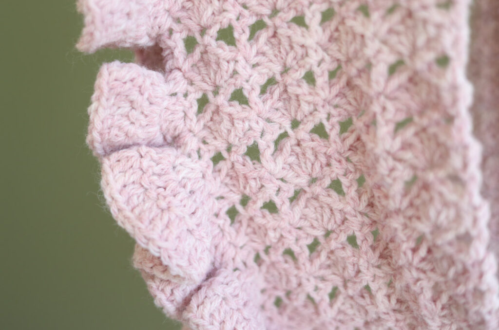 Closeup of a pink crochet lace and ruffle scarf in front of a green wall