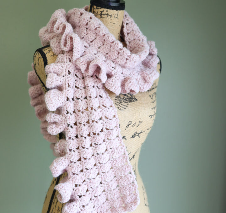 A pink crochet scarf with a ruffle on a dressform in a green room