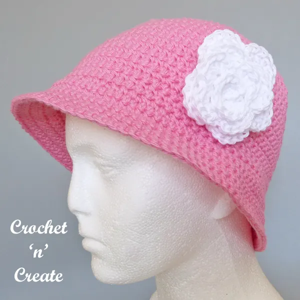 Pink crochet bucket hat with crocheted white flower applique on white mannequin head. 