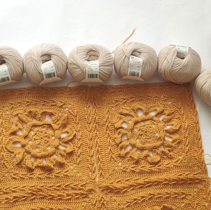 Golden yellow crochet blanket displayed next to cream skeins of yarn on white background. 