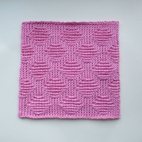 Pink Tunisian diamond crochet square on a white background. 