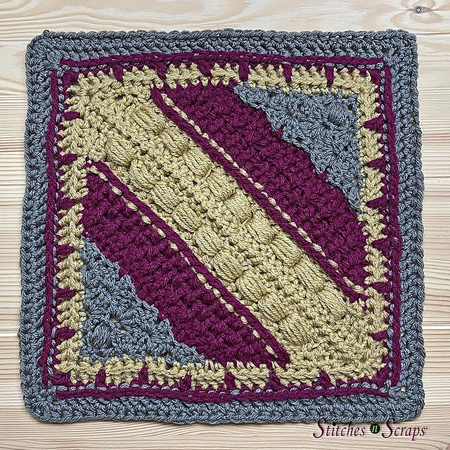 A crocheted, highly textured blue, purple, and green afghan square on a table. 