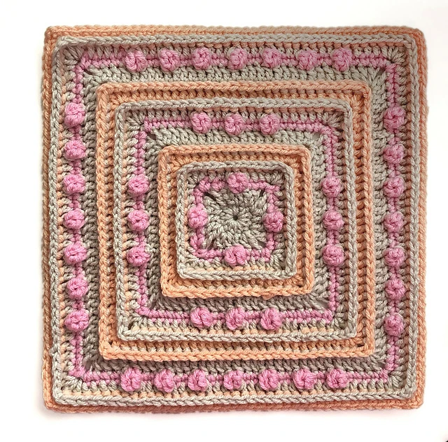 A gray, pink, and light orange afghan texture with a bobbled textured on a white background. 
