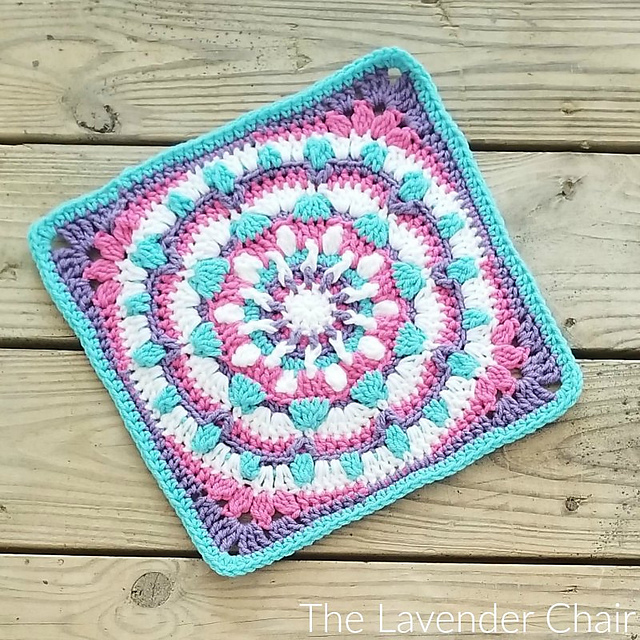 A white, purple, pink and blue crochet mandala afghan square on wood table.