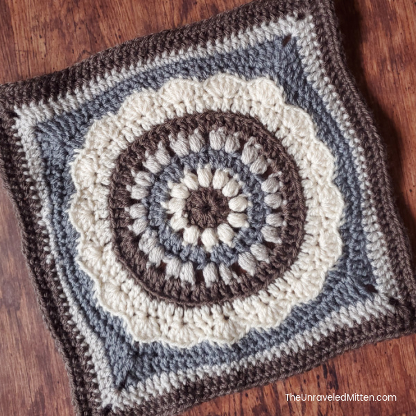 Gray and white crocheted afghan square displayed on wood background. 