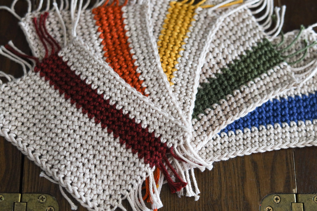 5 mug rug crochet coasters in rainbow stripes laid on a wooden table