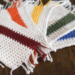 a group of 5 crochet coasters with red orange yellow green and blue stripes