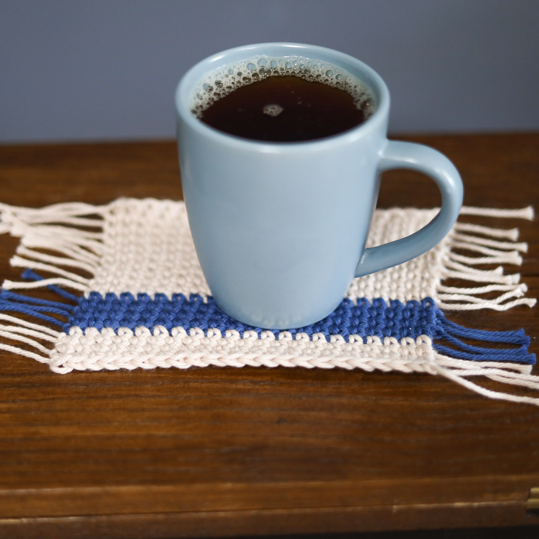 a coffee cup on a crochet coaster with fringe