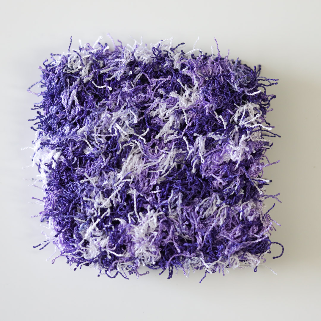 a closeup of a purple and white crocheted dish scrubby