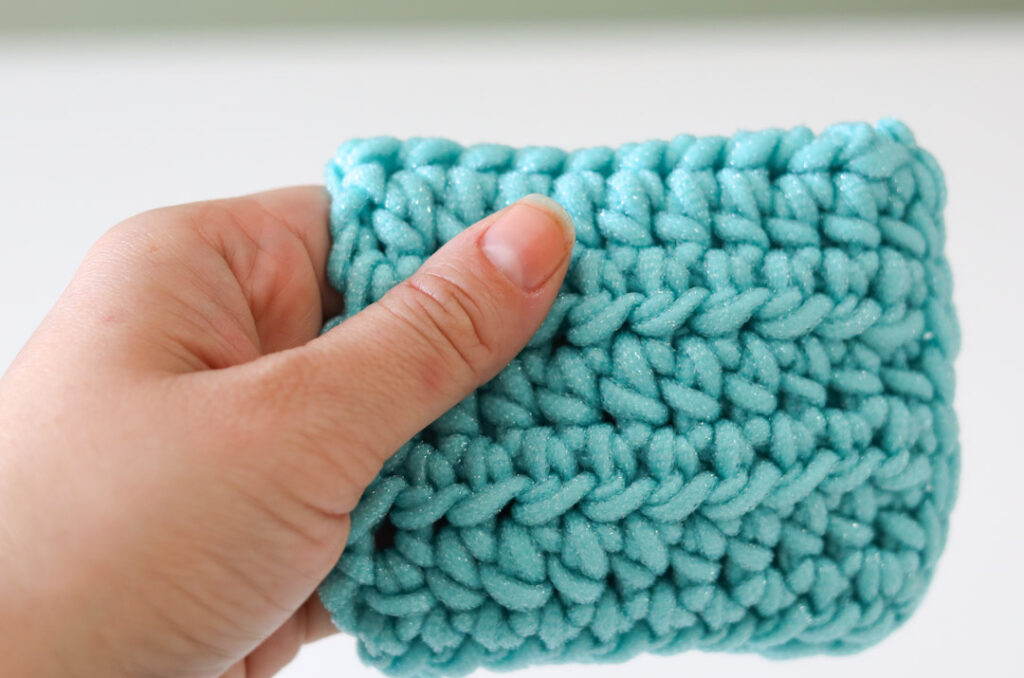 hand holding a small teal scrubby mitt