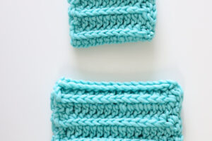 two teal crochet scrubbies laid out on a white table