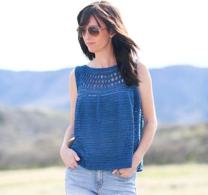 Woman outside wearing sunglasses and  a blue crocheted tank top. 