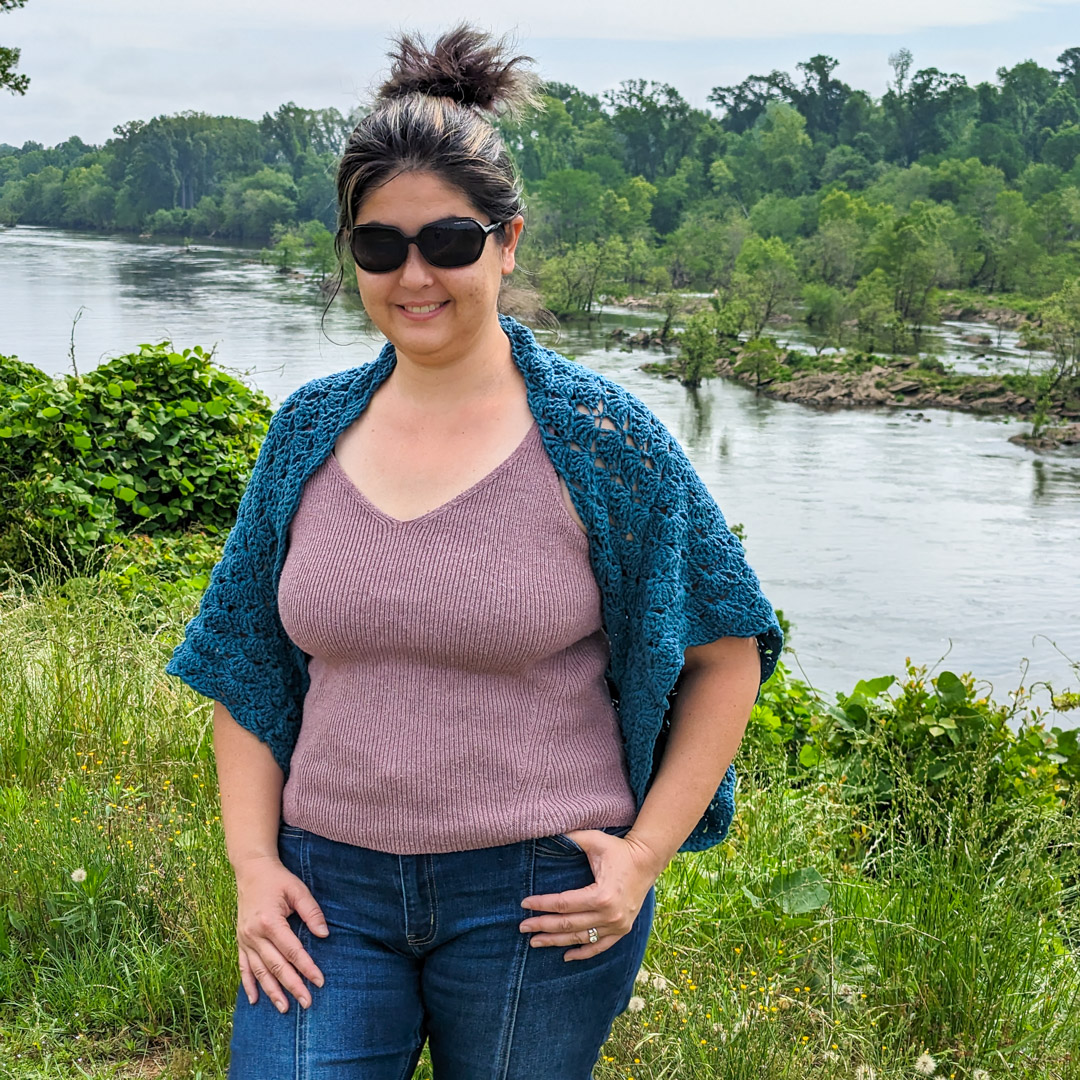 Woman wearing a teal crochet cocoon cardigan in front of a river scenery