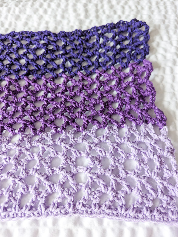 closeup texture shot showing a crochet mesh stitch in 3 shades of purple yarn