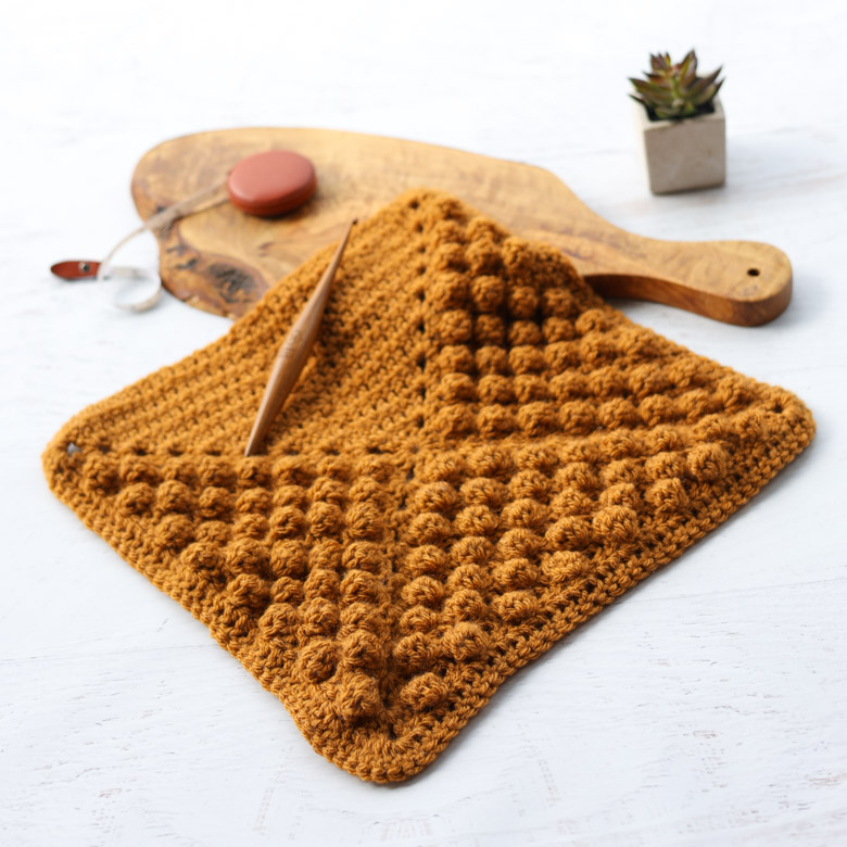 a gold crochet quilt block with bobble stitch texture filling 3/4 of the square