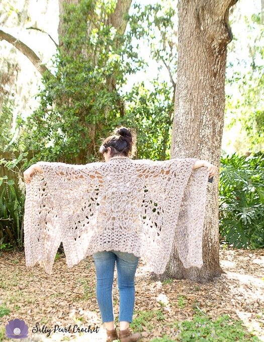 Woman wearing a chunky crochet lace poncho standing outside next to a tree.