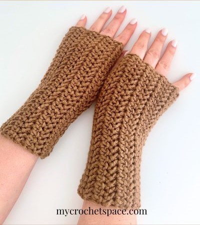A set of hand wearing a pair of tan crochet fingerless mittens.