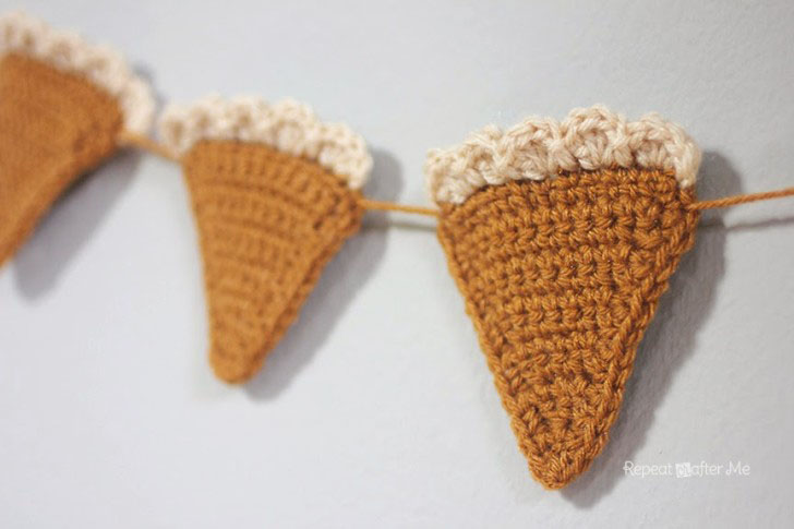 A close up of crochet pumpkin pie bunting hanfing on a wall