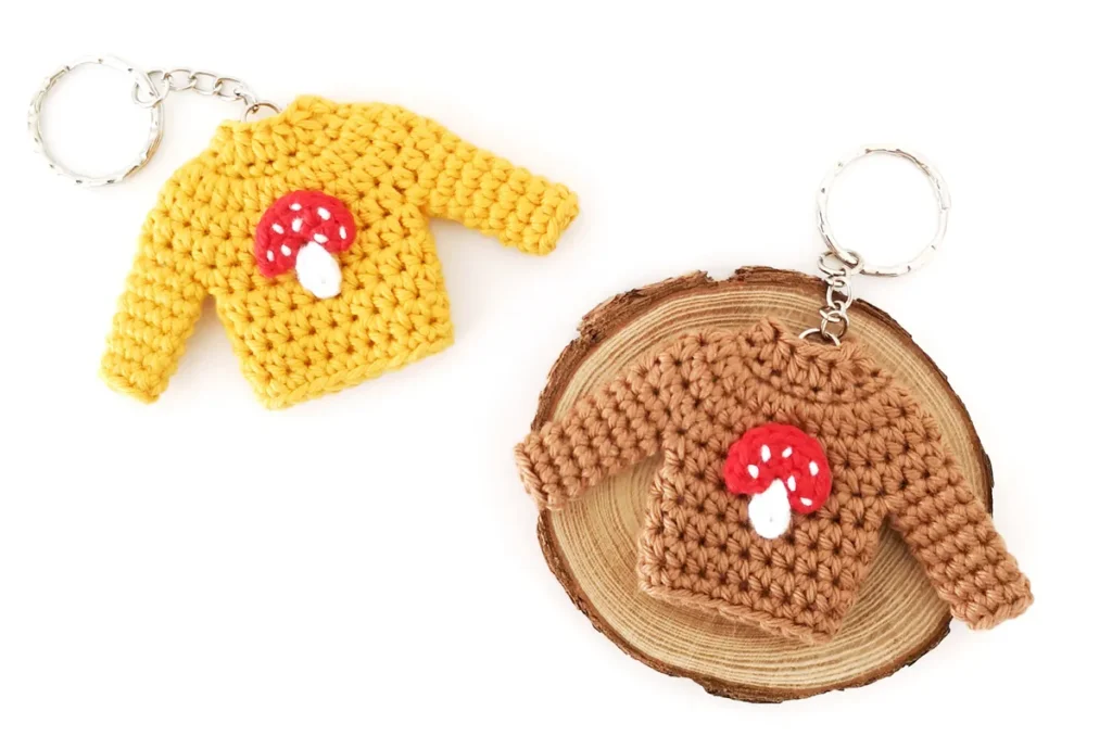 Two crochet mushroom sweater keychains displayed on a white background.
