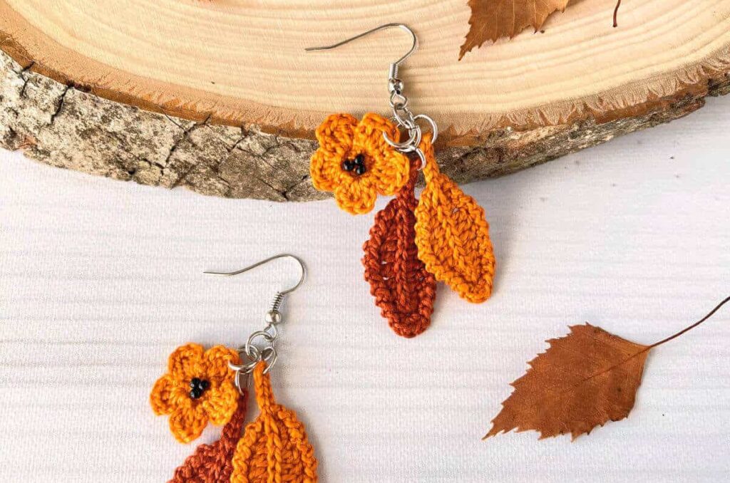 A pair of crochet leaf earrings in a golden yellow and burnt orange color.