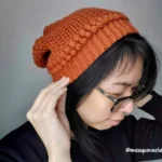 Woman wearing a burnt orange crochet beanie.