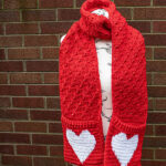 Red crochet scarf with pockets and white hearts on the pockets, displayed on a mannequin.